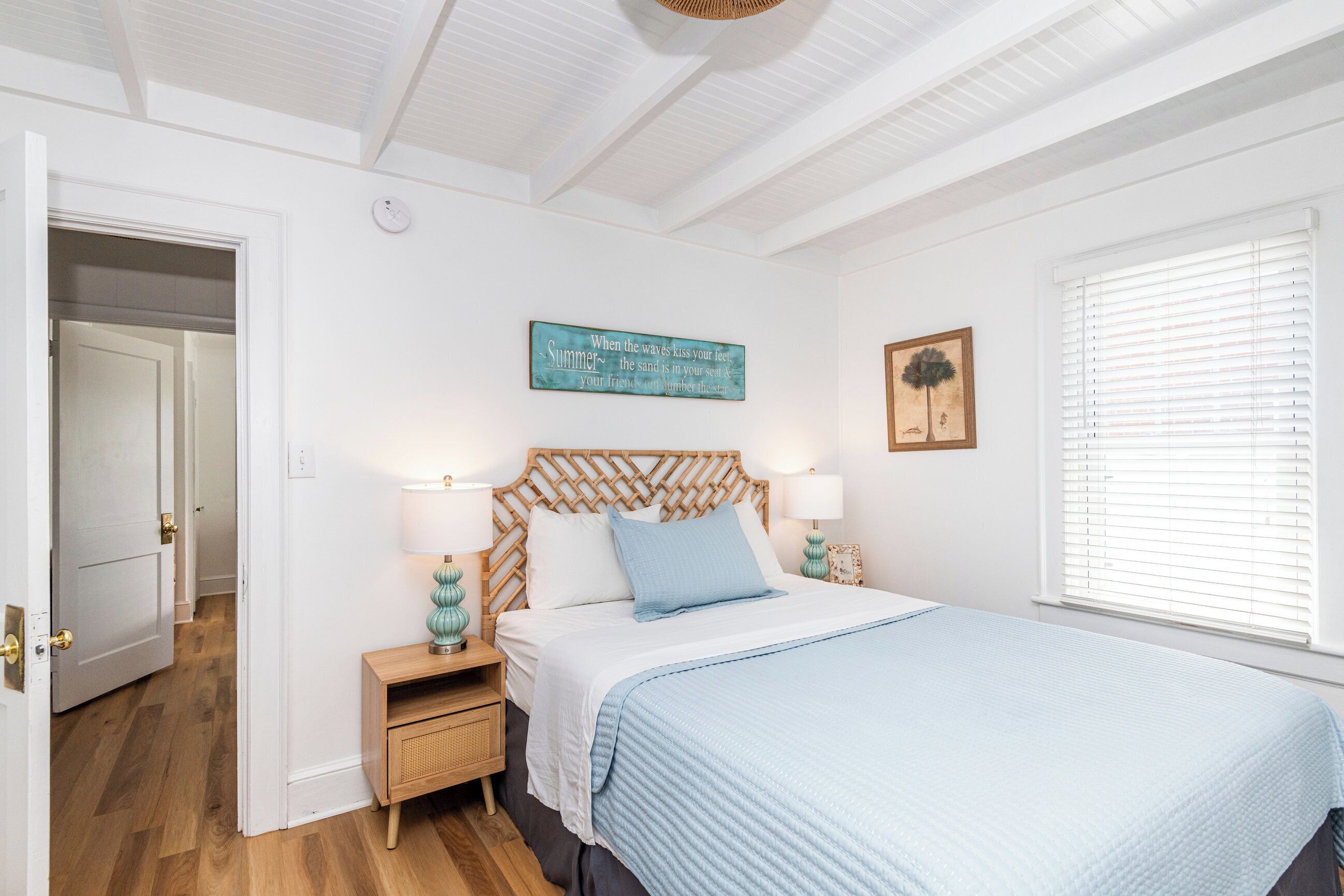 A bedroom with a wooden headboard, a bed with a blue blanket, two bedside lamps, a wall clock, and a window with blinds.
