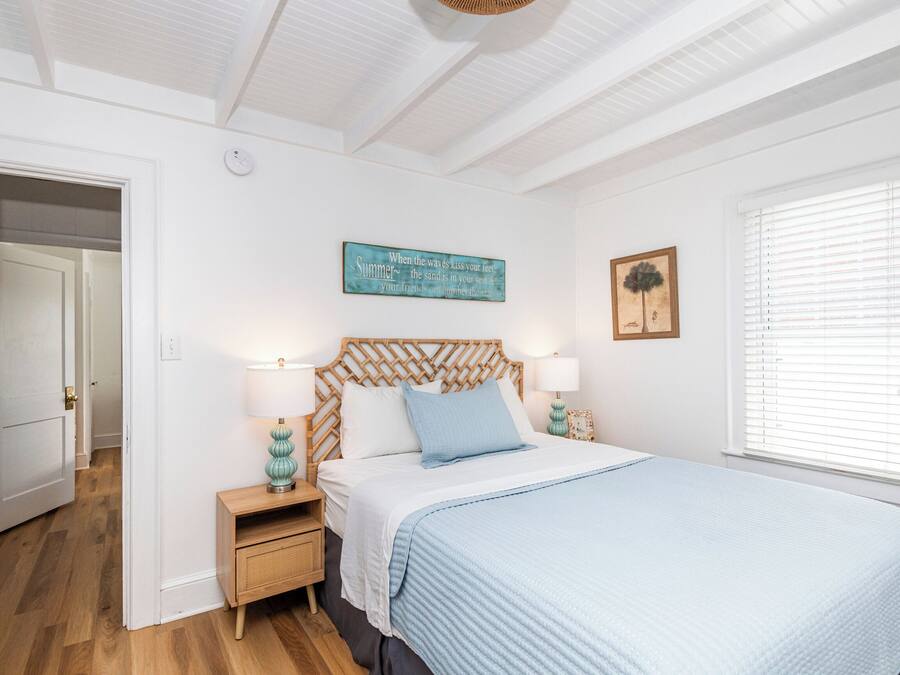 A bedroom with a wooden headboard, a bed with a blue blanket, two bedside lamps, a wall clock, and a window with blinds.
