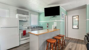A kitchen with a central island, bar stools, a microwave, and a television mounted on the wall. - Island Guesthouse and Motel (Manteo)