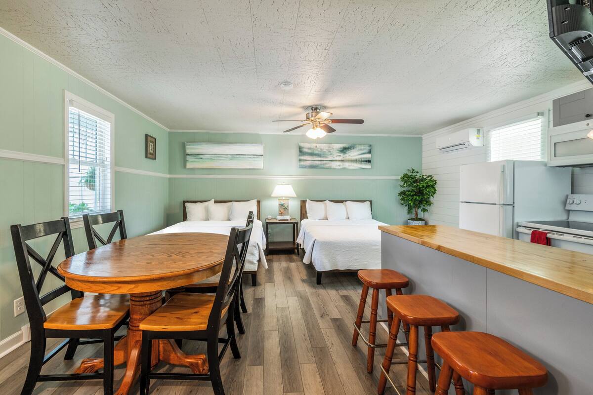 Une chambre d’hôtel compacte comprenant une table à manger, deux lits, un coin cuisine et un ventilateur de plafond.