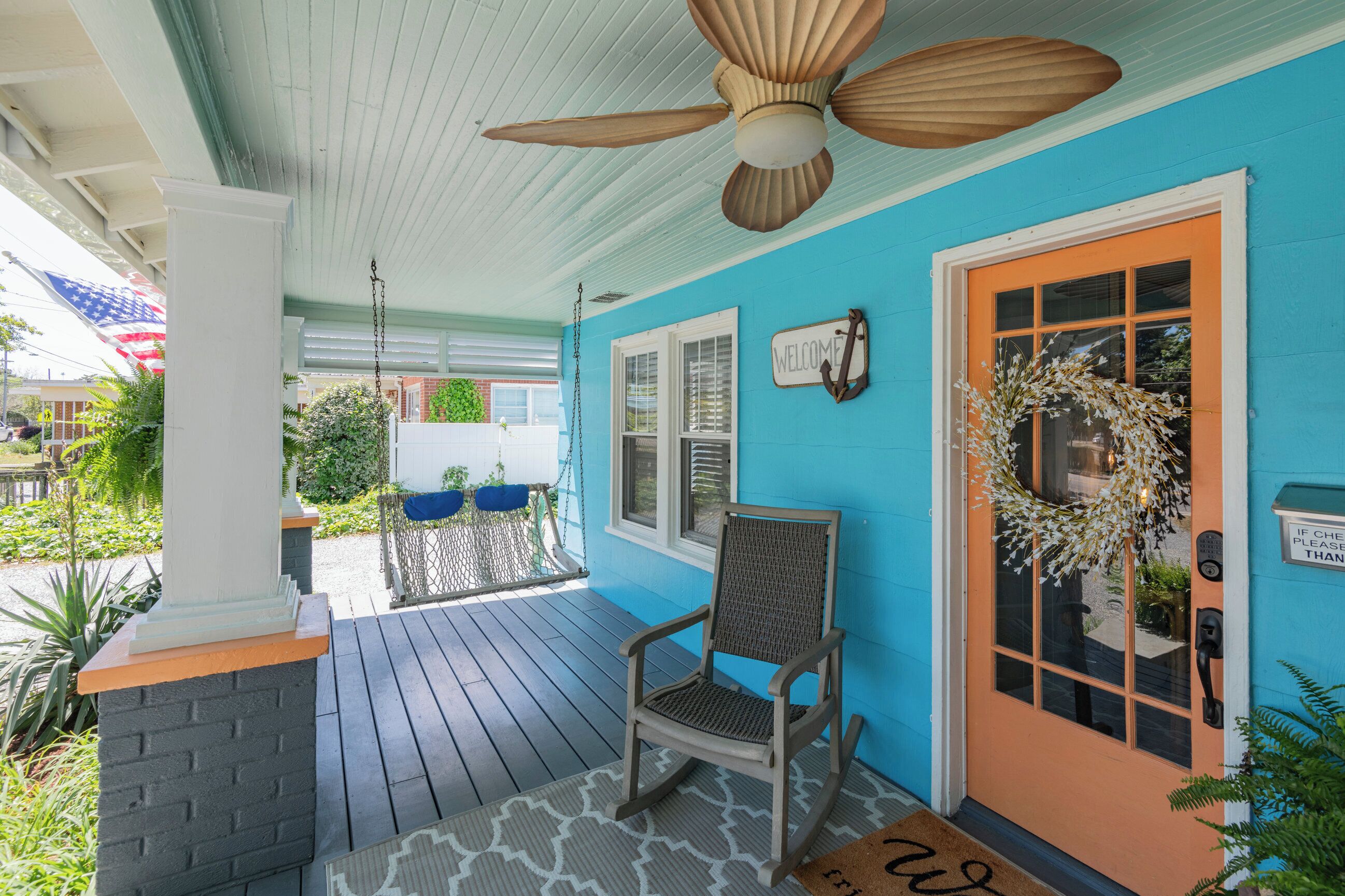 A porch with a ceiling fan, a rocking chair, a welcome sign, and a door with a wreath.