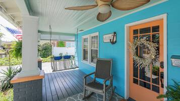A porch with a ceiling fan, a rocking chair, a welcome sign, and a door with a wreath.