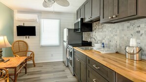 A kitchen with dark cabinets, a wooden countertop, a microwave, a sink, and a ceiling fan. - Island Guesthouse and Motel (Manteo)