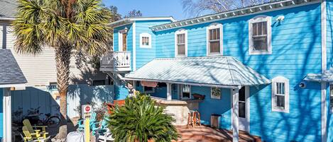 A two-story blue house with a porch, outdoor seating, and a stop sign indicating a fire pit ahead.