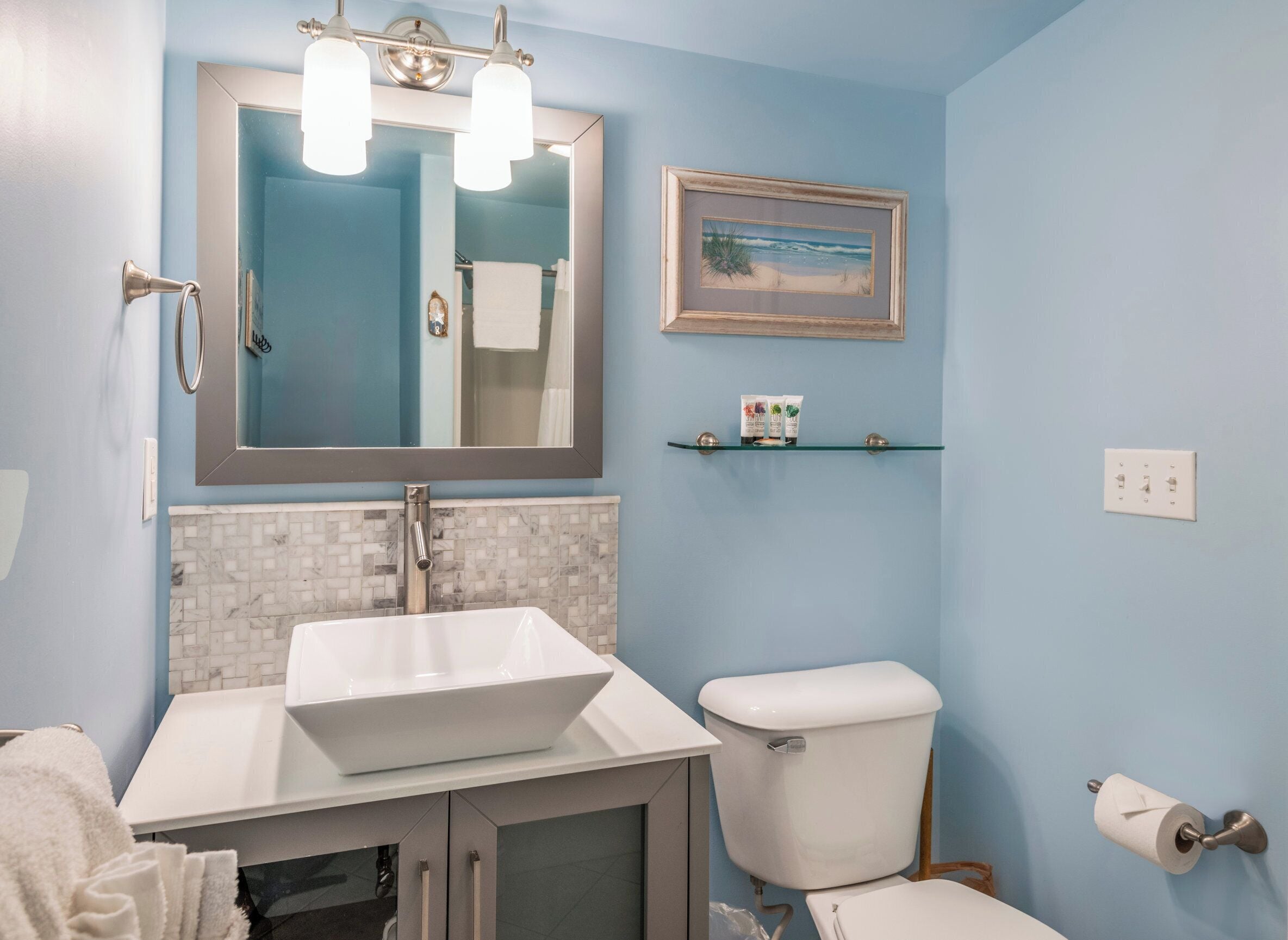 A bathroom with a white sink, a toilet, a mirror, and a shelf with toiletries.