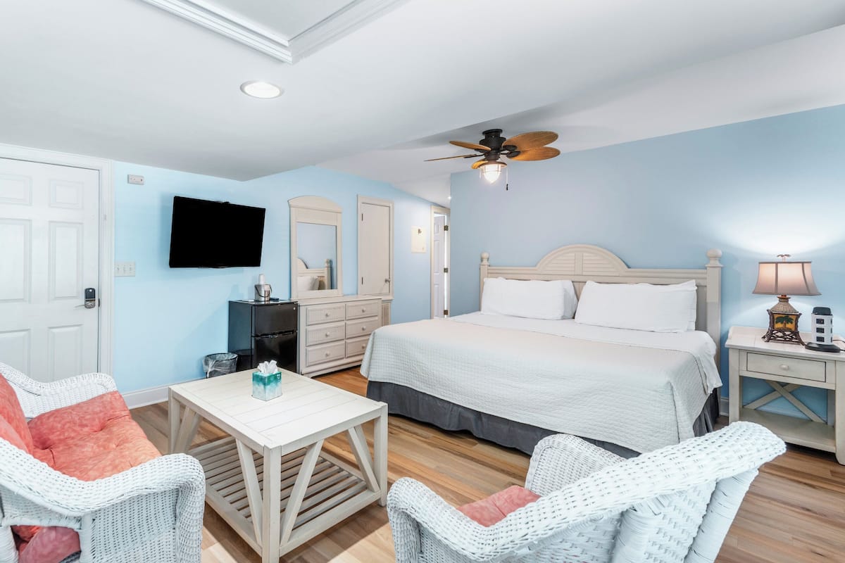 Une chambre à coucher comprenant un lit, un téléviseur, un ventilateur de plafond, une commode et des chaises en osier.