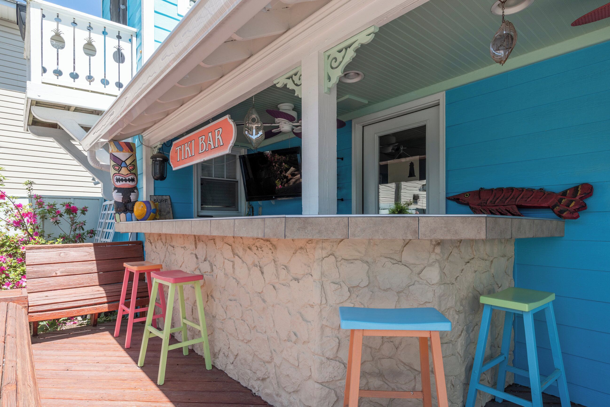 Un bar tiki con taburetes de colores, una barra de piedra y un pez decorativo en la pared.