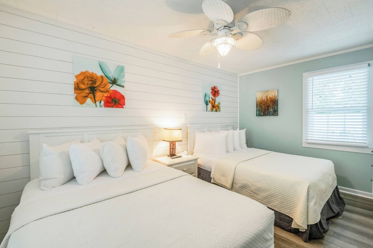 Une chambre avec deux lits, un ventilateur de plafond et des œuvres d’art accrochées aux murs.