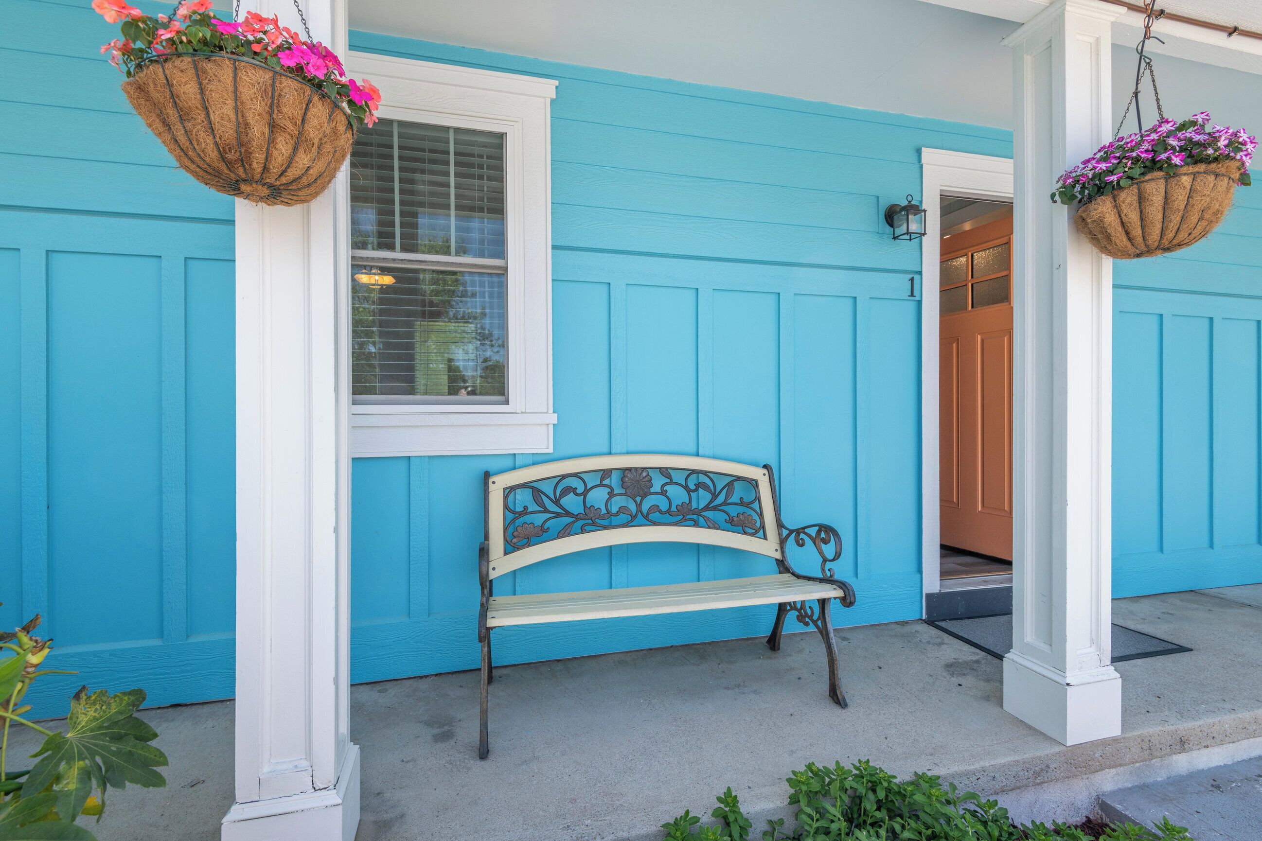 Ein blaues Haus mit einer Bank und blumengeschmückten Körben.