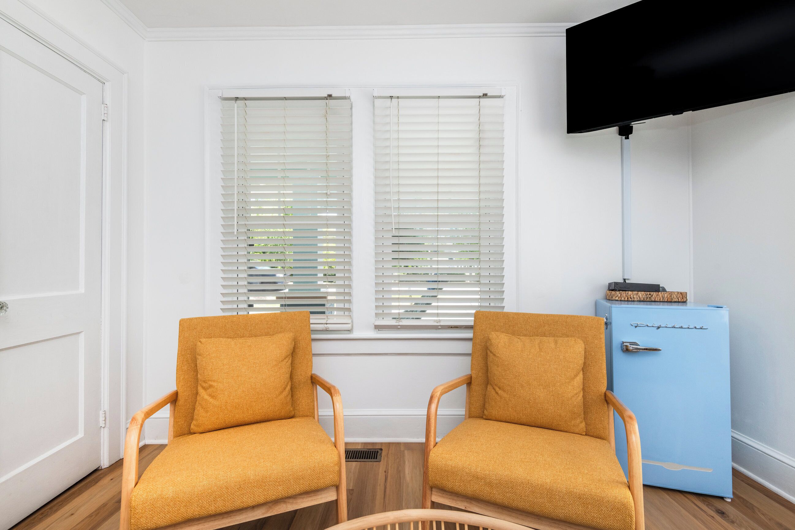 A room with two wooden chairs, a blue cabinet, and a television mounted on the wall.
