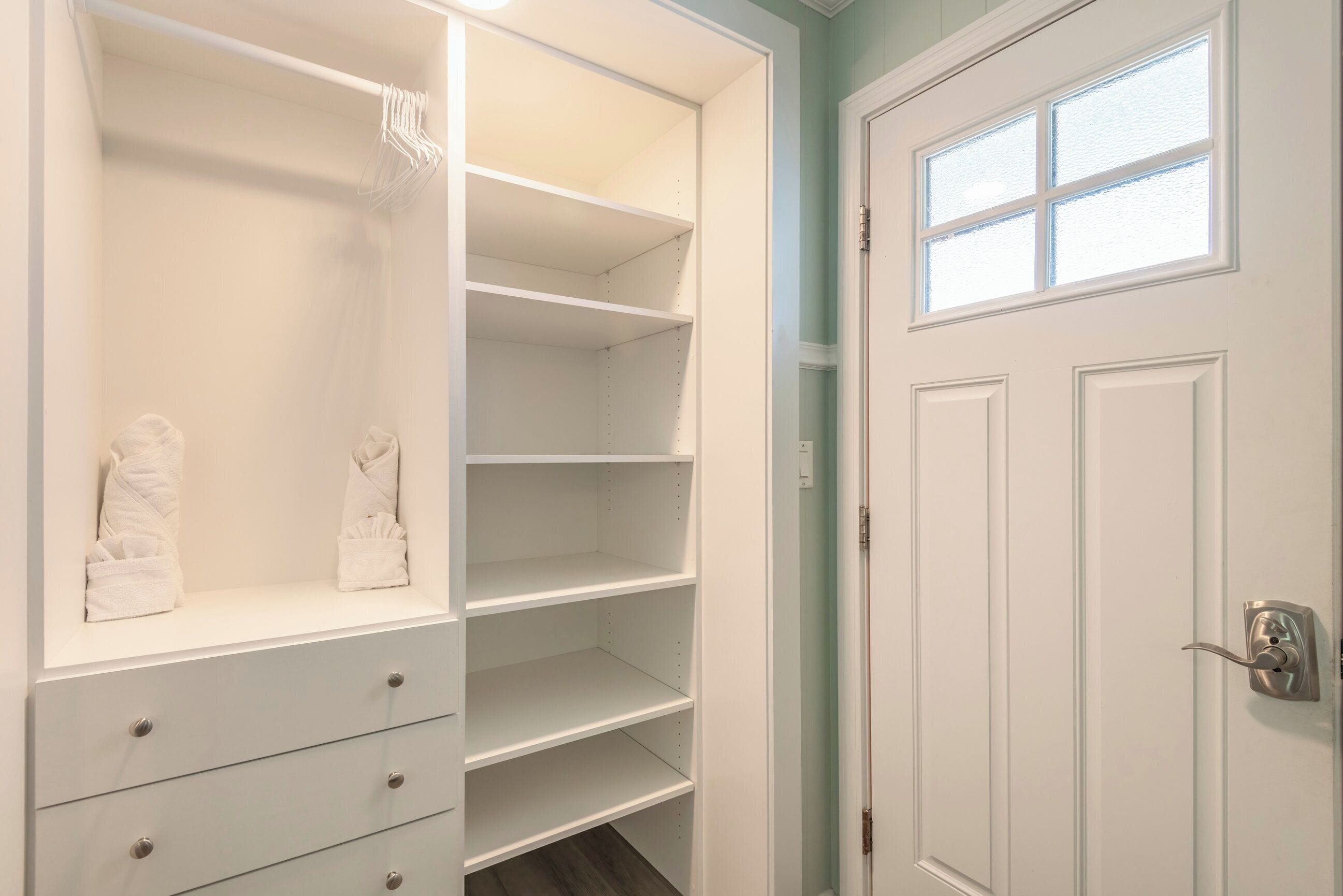 A walk-in closet with open shelves and drawers, a door with a window, and a light switch on the wall.
