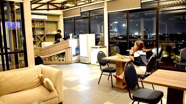A modern interior with a sofa, dining table, chairs, and a kitchen area with a person preparing food. - Aruuman Hotel Simpanglima Semarang (Semarang)