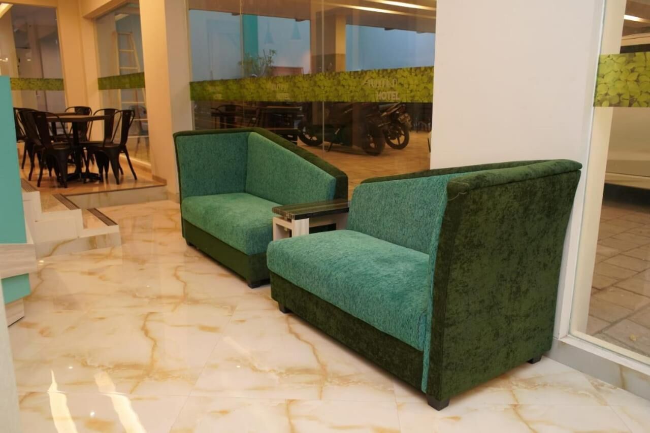 En modern hotellobby med grönt klätt möblemang, ett marmorgolv och utsikt över matsalen genom glasdörrar.
