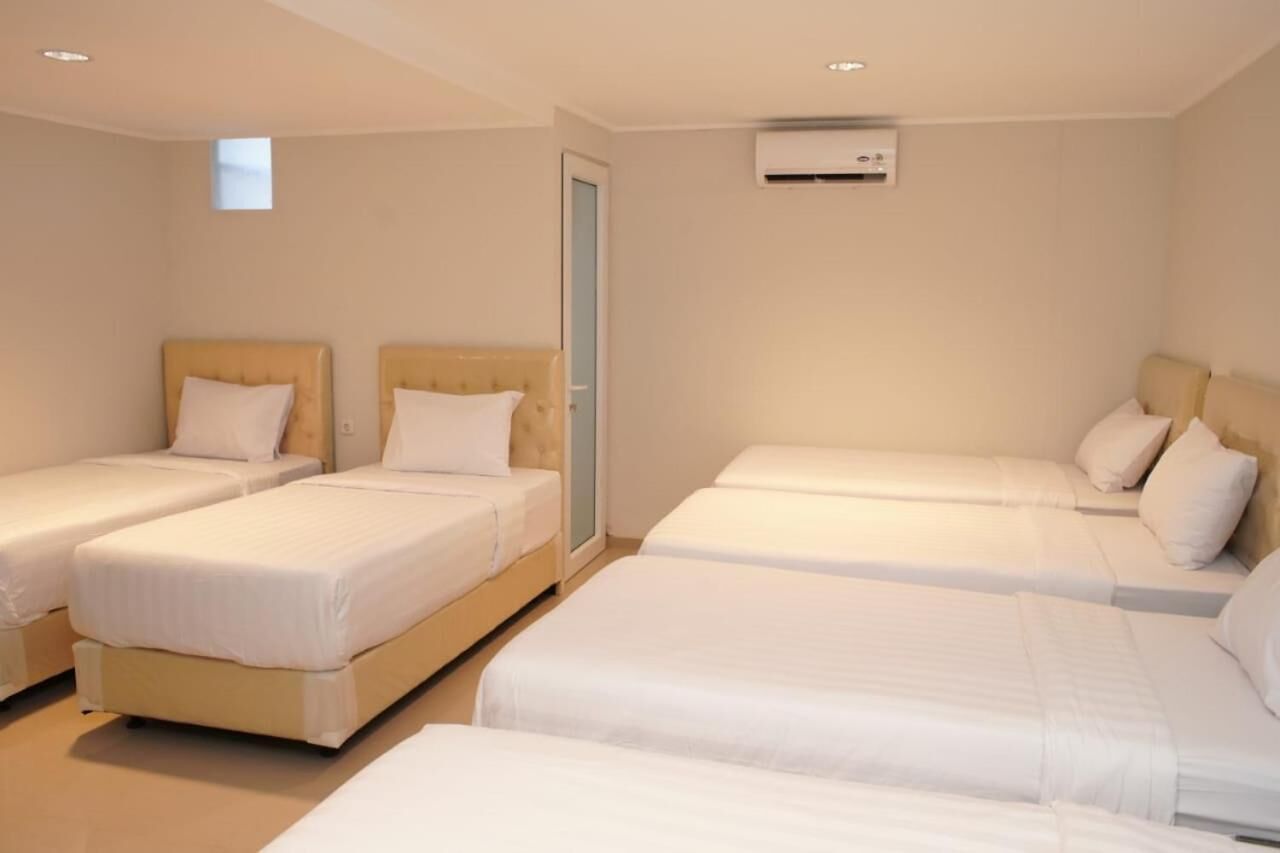 A hotel room with three single beds, a window, and an air conditioning unit.