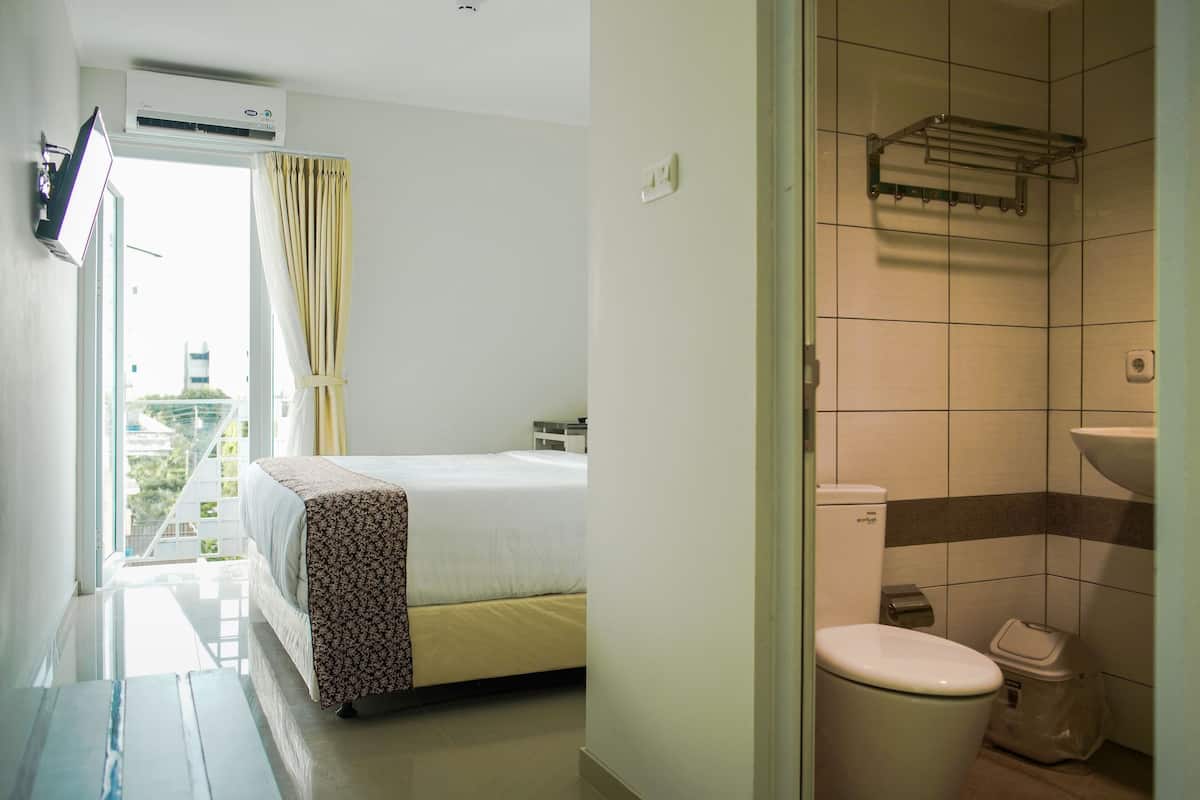 A hotel room with a bed, a bathroom with a toilet and sink, and a view of buildings outside.