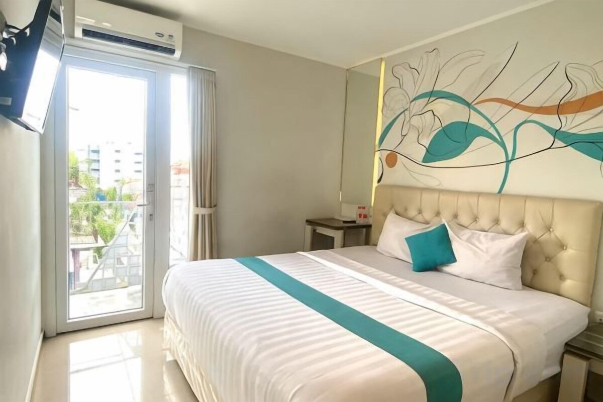 A hotel room with a large bed, a nightstand, a wall-mounted TV, and a sliding glass door to the outside.