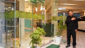 A hotel entrance with a reception desk, a glass elevator, and potted plants. - Aruuman Hotel Simpanglima Semarang (Semarang)