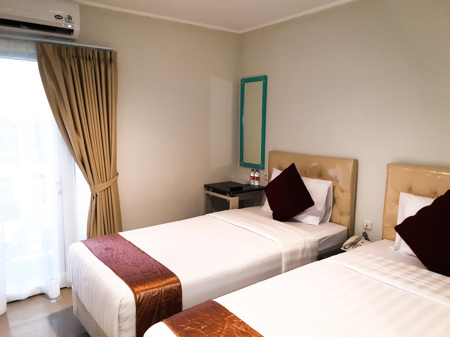 A hotel room with two beds, a nightstand, a mirror, and an air conditioning unit.