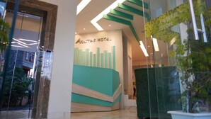A modern hotel lobby with a prominent reception desk and a staircase leading to upper floors. - Aruuman Hotel Simpanglima Semarang (Semarang)