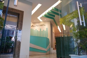 A modern hotel lobby with a prominent reception desk and a staircase leading to upper floors.