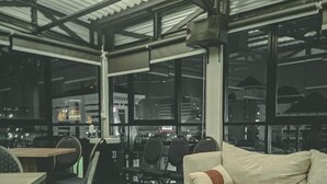 A covered outdoor seating area with a checkered floor, a wooden coffee table, a sofa, and a chair. - Aruuman Hotel Simpanglima Semarang (Semarang)