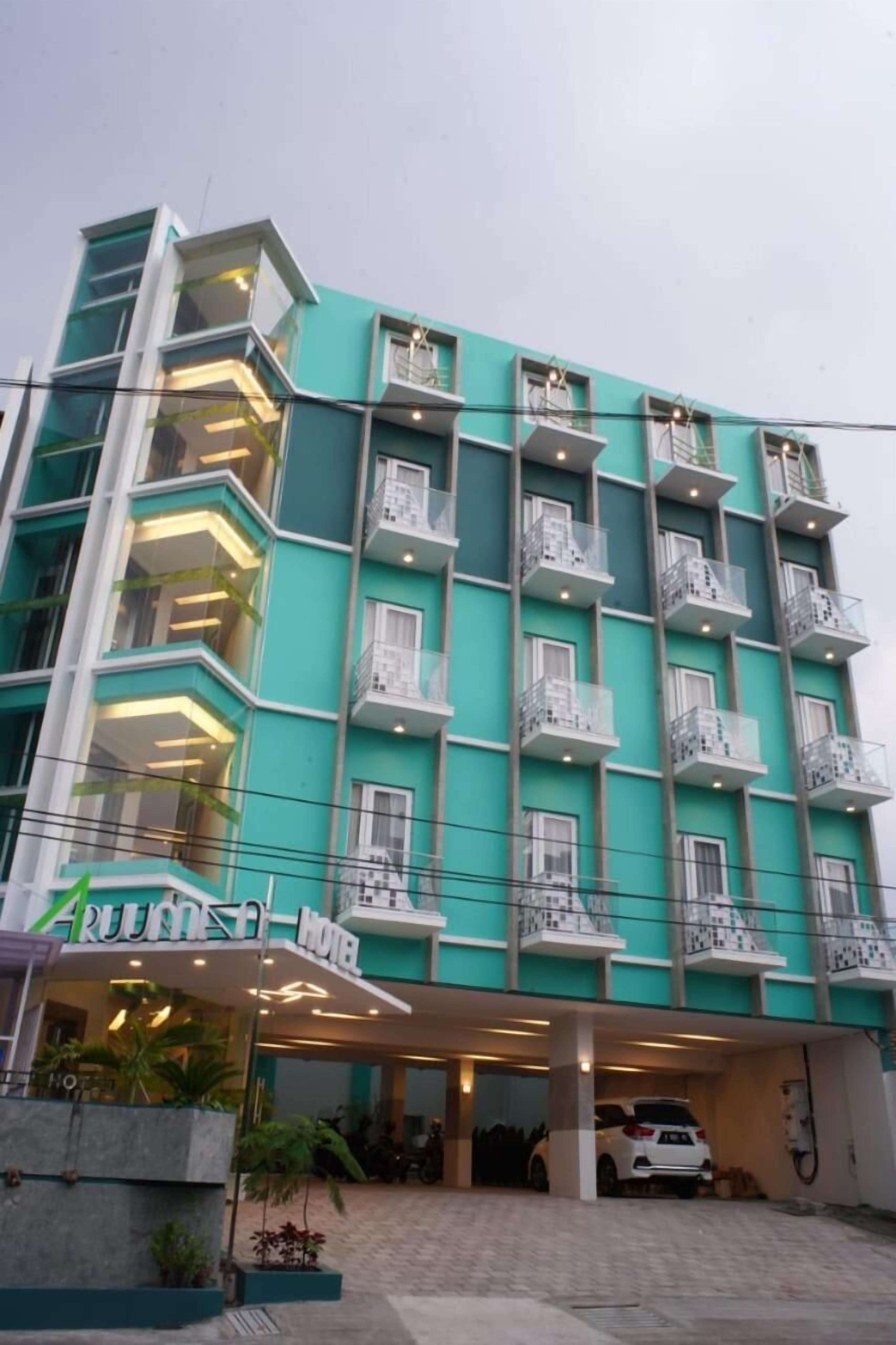 Un hôtel à plusieurs étages, doté d’une façade de couleur turquoise, de balcons et d’une entrée couverte.