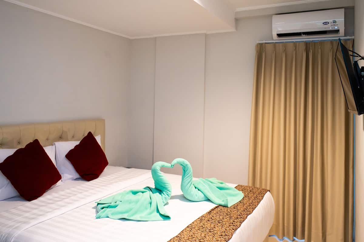 A hotel room with a bed, a headboard, a wall-mounted air conditioner, and a curtain.