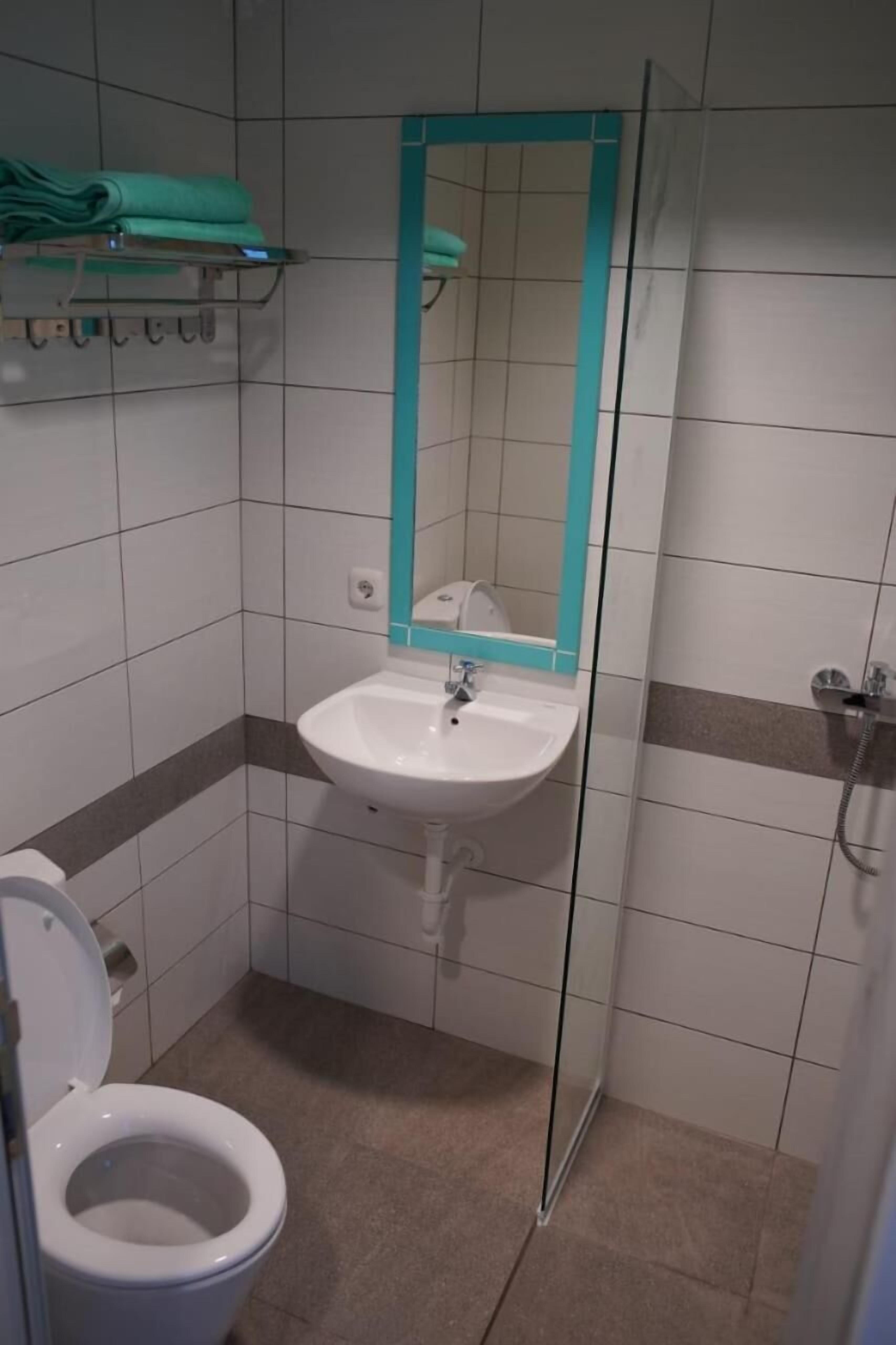 Un baño pequeño con un lavamanos blanco, un espejo con marco color turquesa, un inodoro y una zona de ducha.