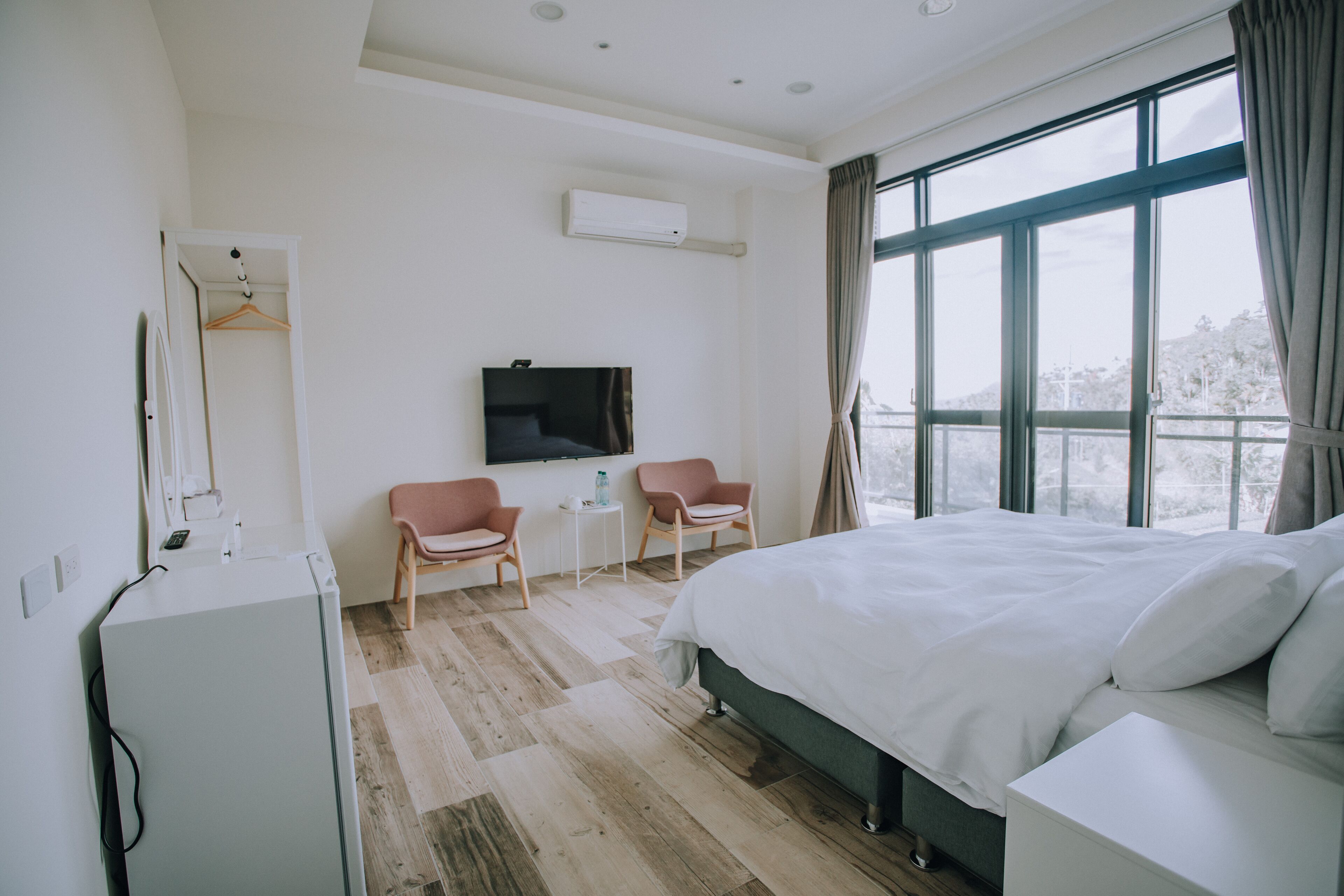 A hotel room with a large bed, two chairs, a small table, a TV, and a window with a view.