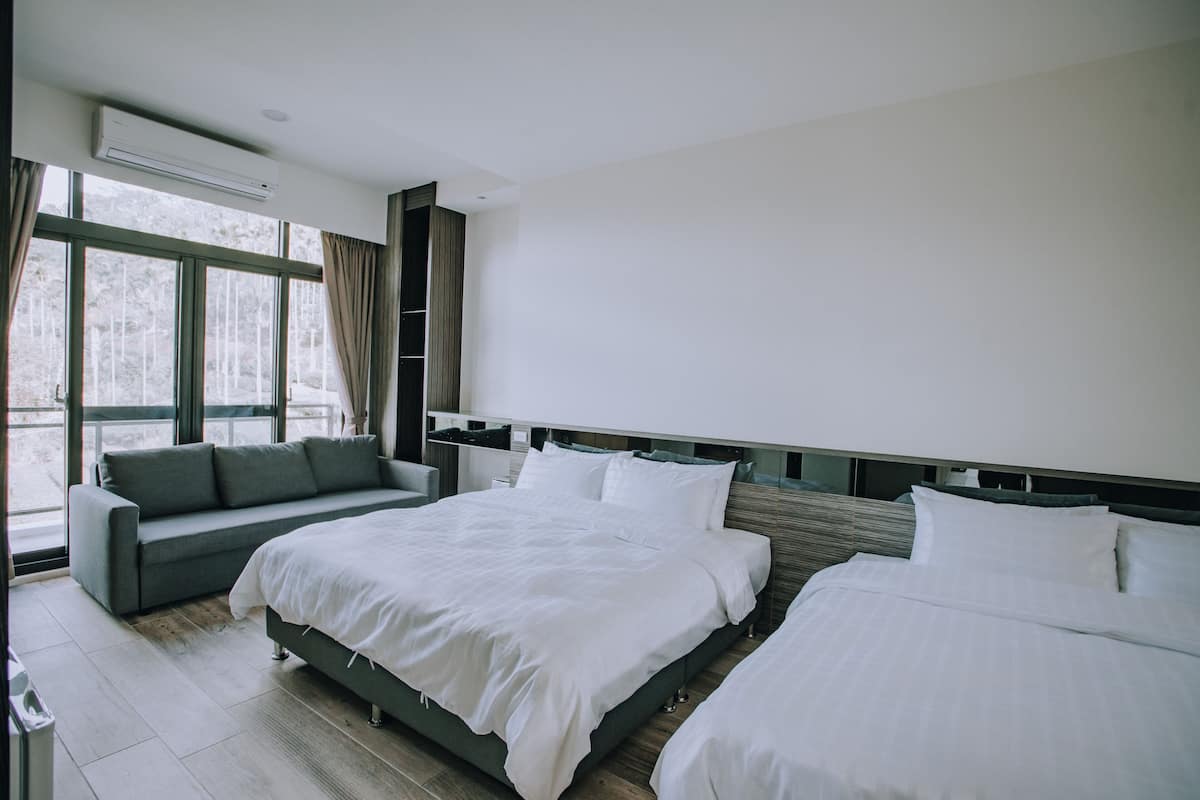 A modern hotel room with two beds, a sofa, and a large window with curtains.