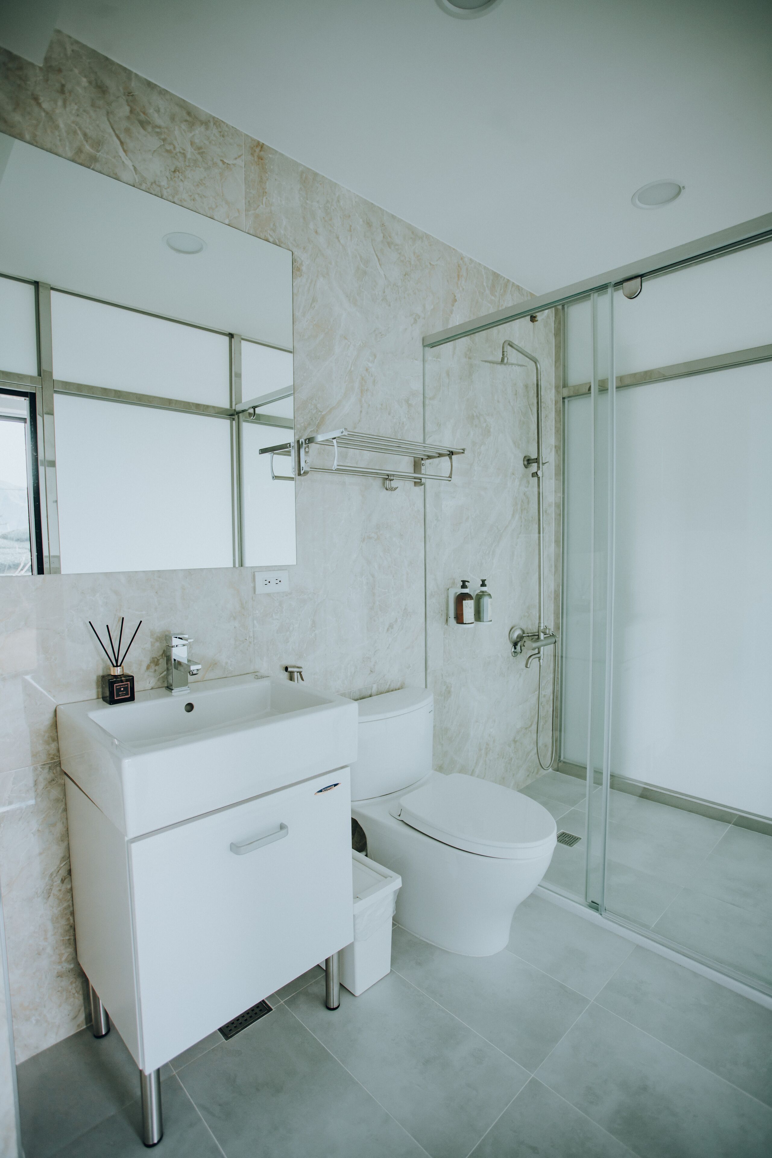 A modern bathroom with a white vanity, a glass shower enclosure, and a marble wall.