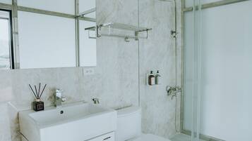 A modern bathroom with a white vanity, a glass shower enclosure, and a marble wall.