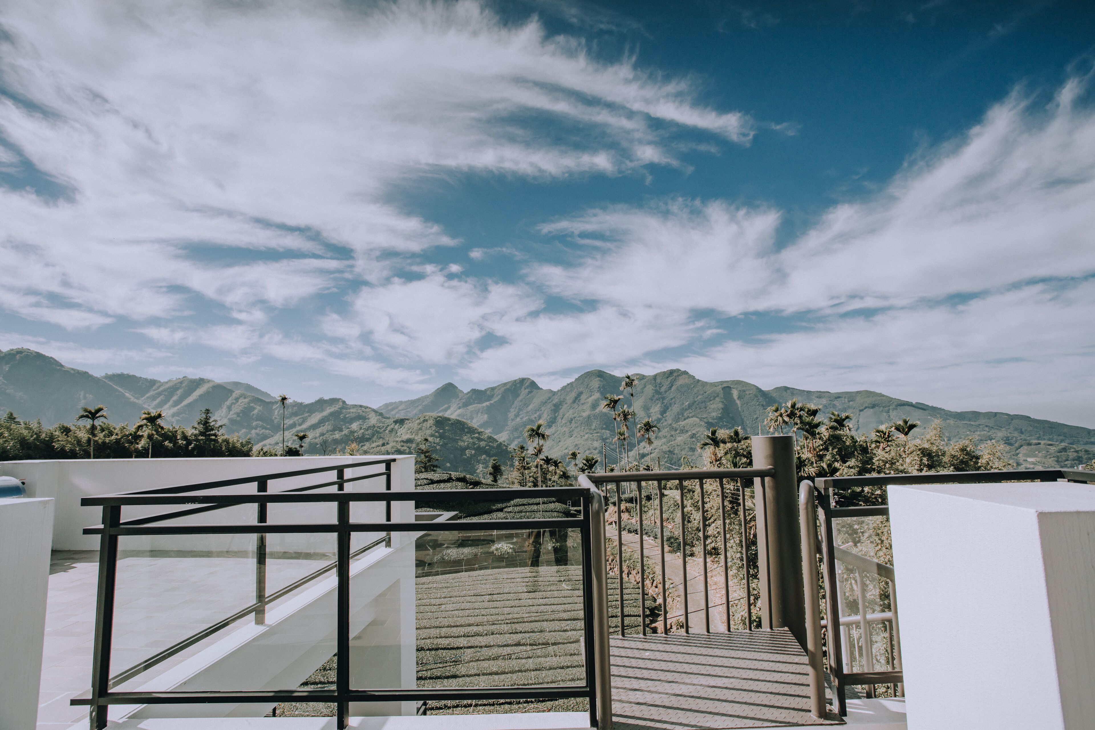 A modern staircase leading to a terrace with a view of mountains and palm trees under a partly cloudy sky.