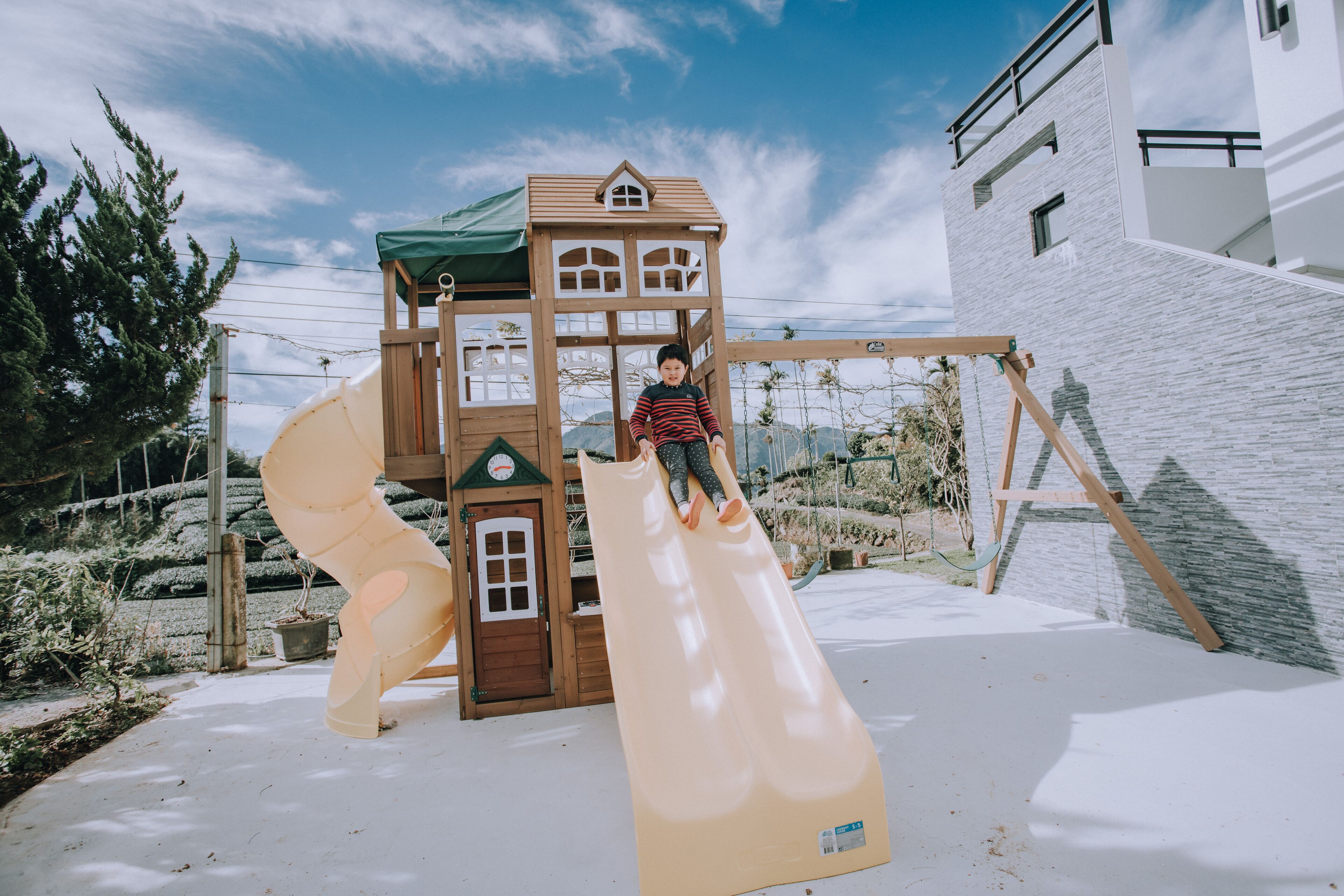 Un terrain de jeux avec un toboggan et des structures d’escalade, situé devant un bâtiment moderne et sous un ciel dégagé.