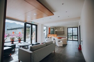 Un interior moderno con sofá, mesa de comedor y sillas, ventanas amplias con vistas a montañas, y una zona de cocina.