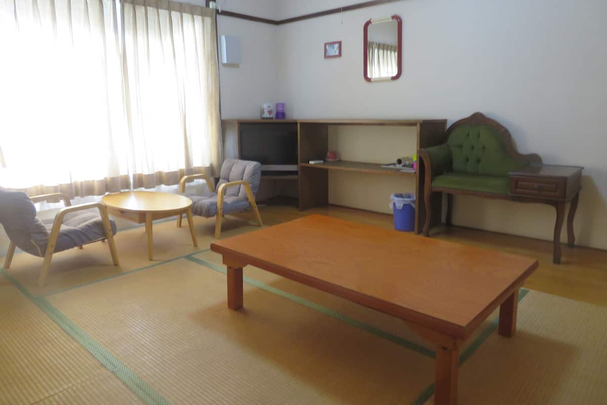 A living room with tatami flooring, a low table, a sofa, and a television.