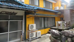 Un bâtiment jaune à l’architecture traditionnelle, avec un toit en tuiles et plusieurs unités de climatisation.