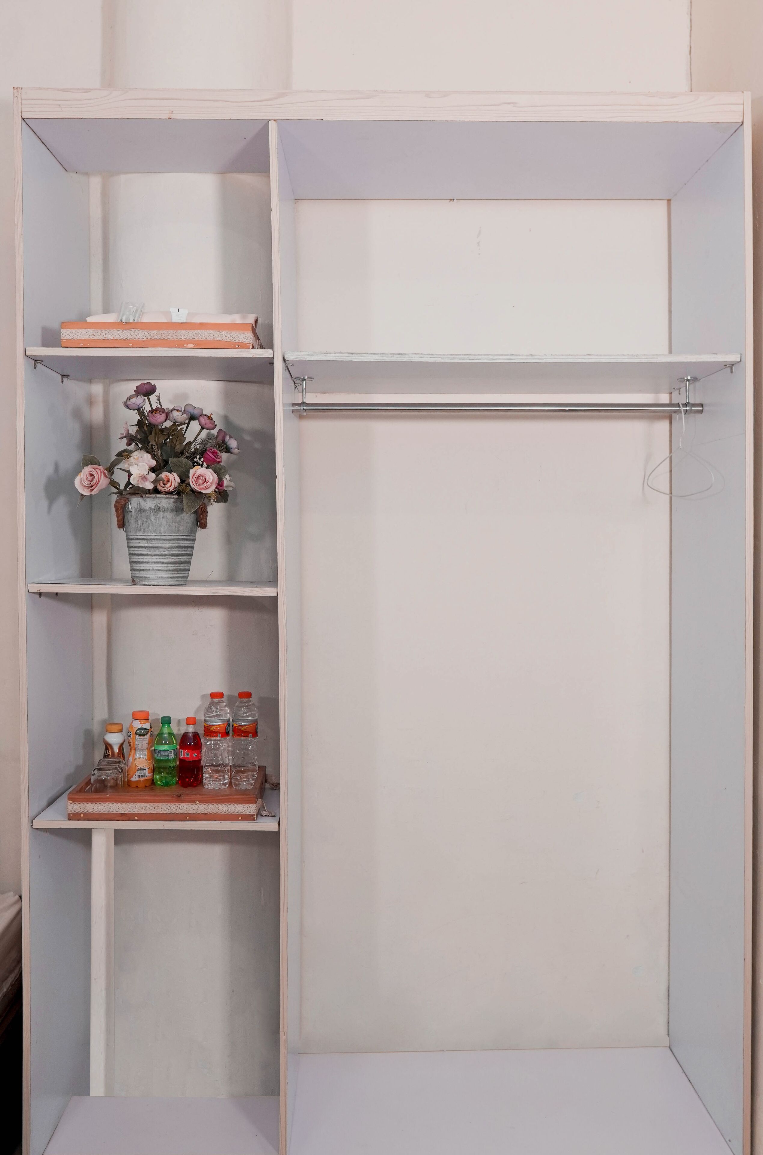 A white wardrobe with multiple shelves, one of which holds a metal bucket with flowers and bottles.