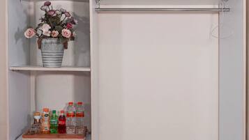 Ein weißer Kleiderschrank mit mehreren Einlegeböden, auf einem davon befindet sich ein Metallkübel mit Blumen und Flaschen.