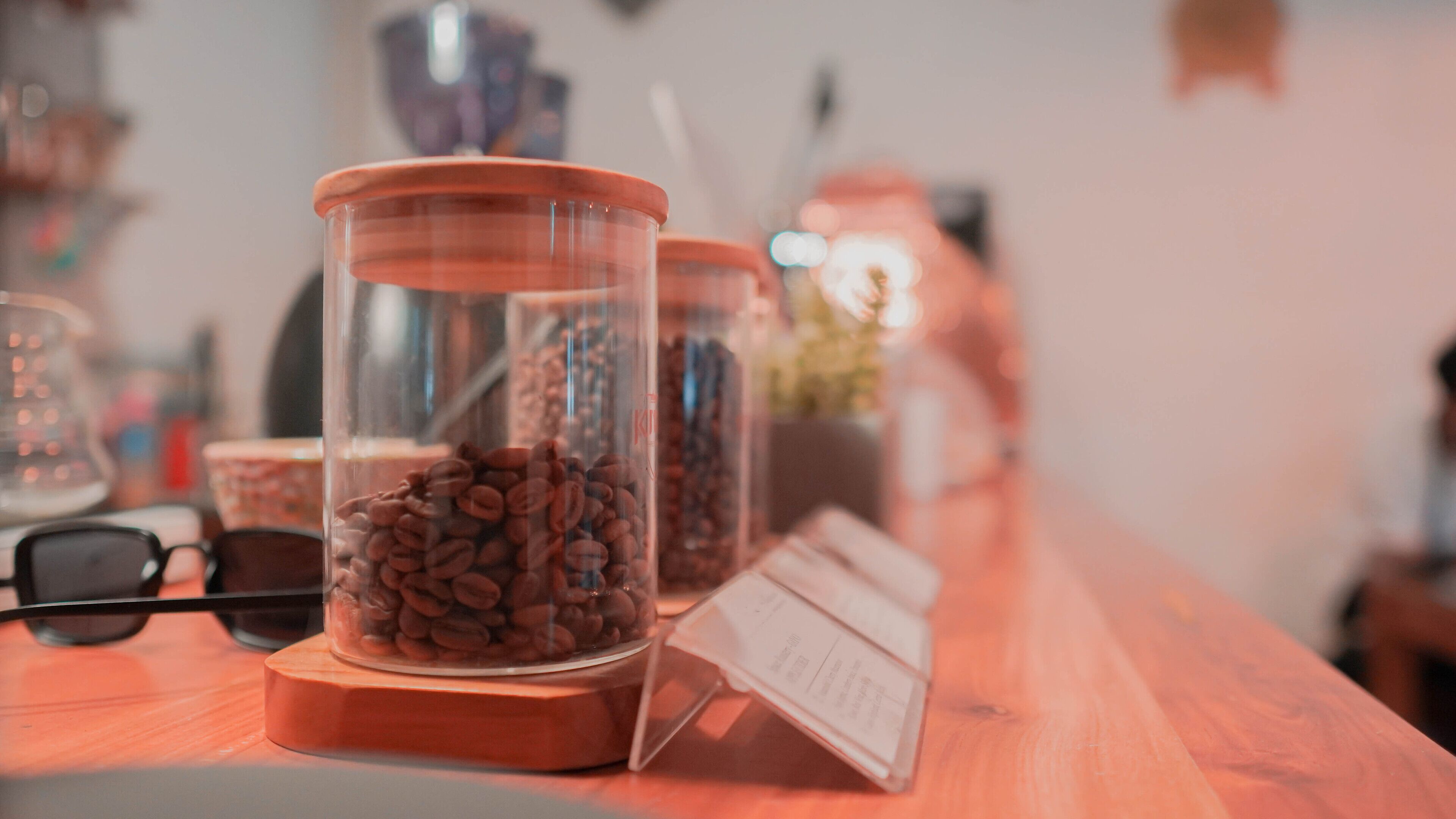 A wooden counter with two glass jars filled with coffee beans, a pair of glasses, and a menu.