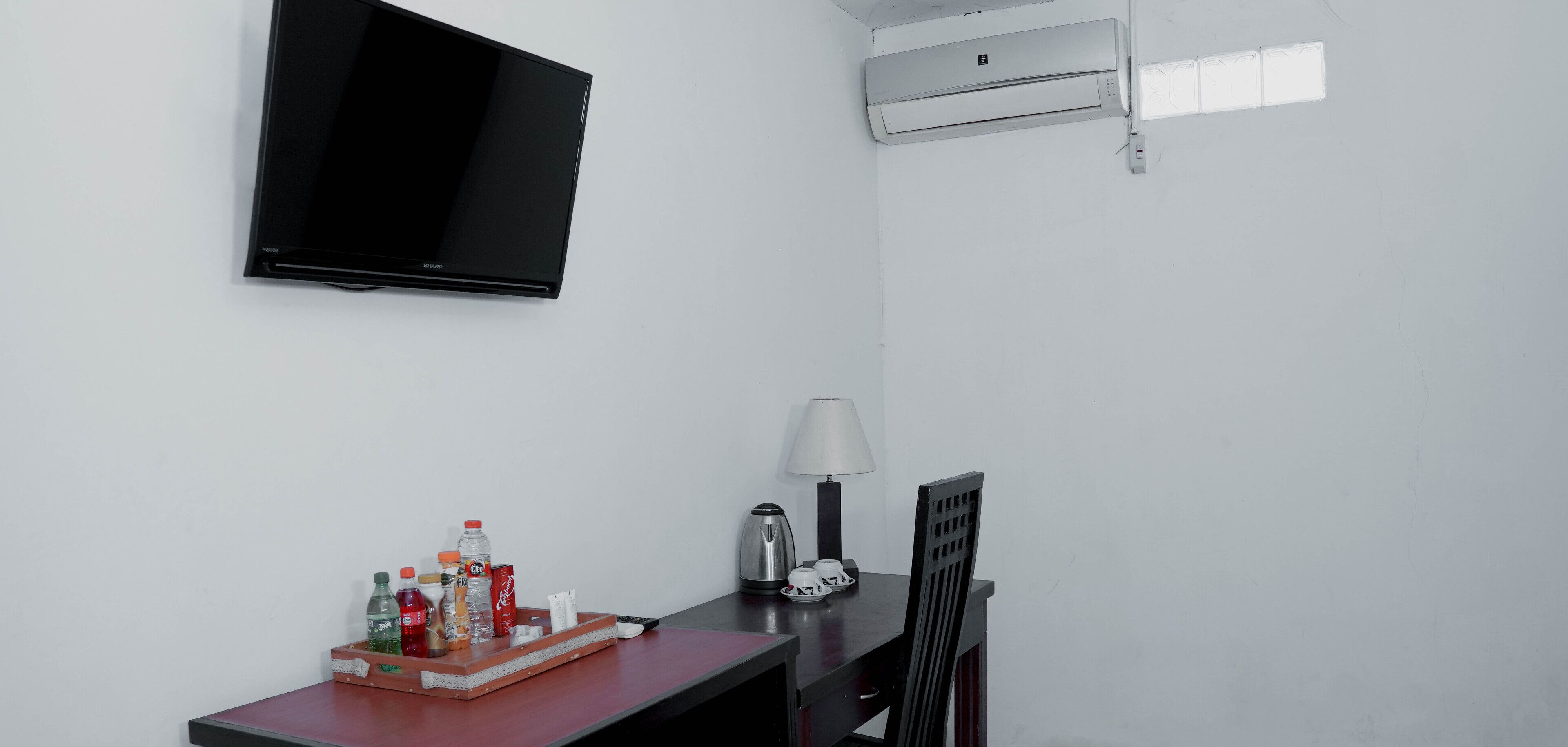 A hotel room with a flat-screen TV mounted on the wall, a table with a tray of beverages, a lamp, and a coffee maker.