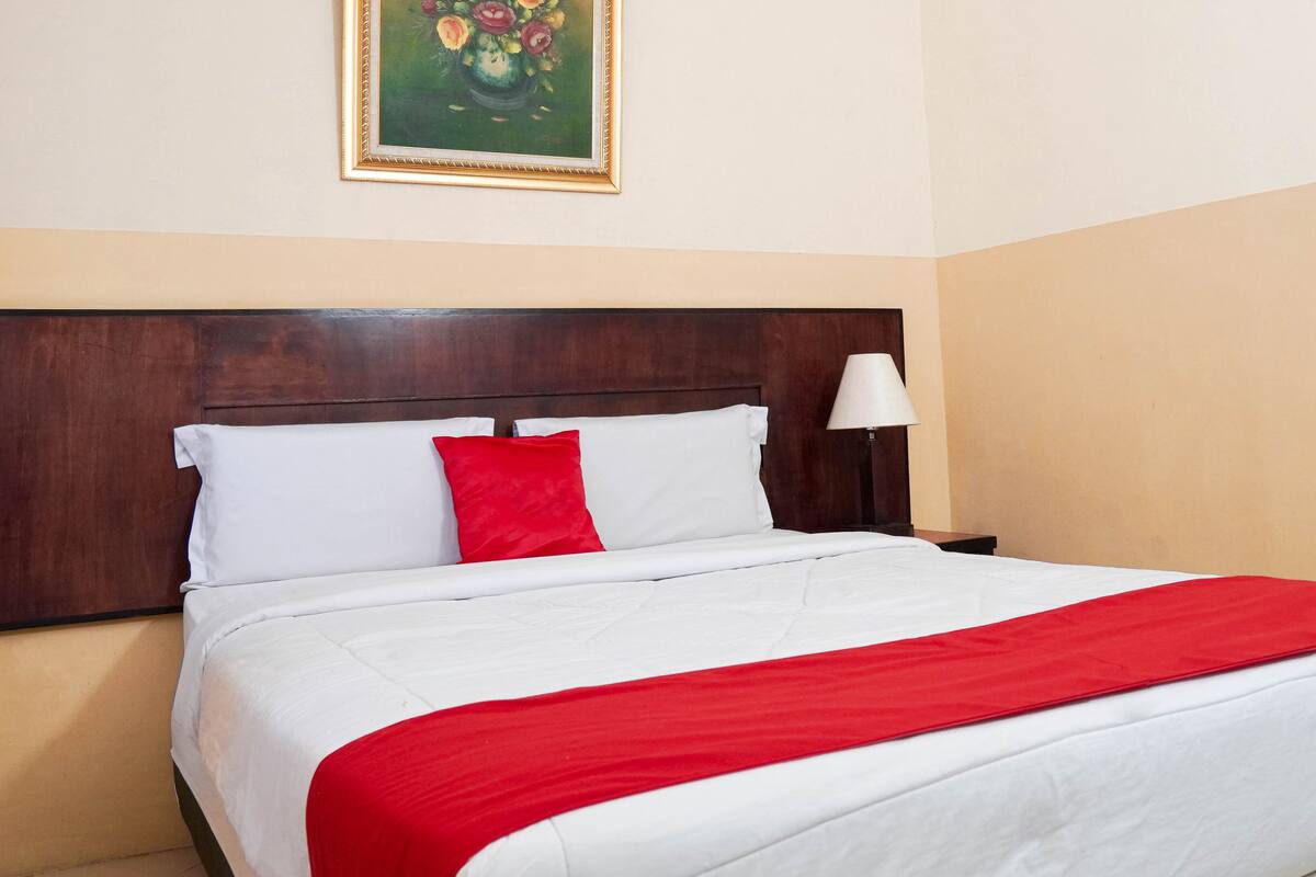 A neatly made bed with white and red bedding, a wooden headboard, and a single bedside lamp.