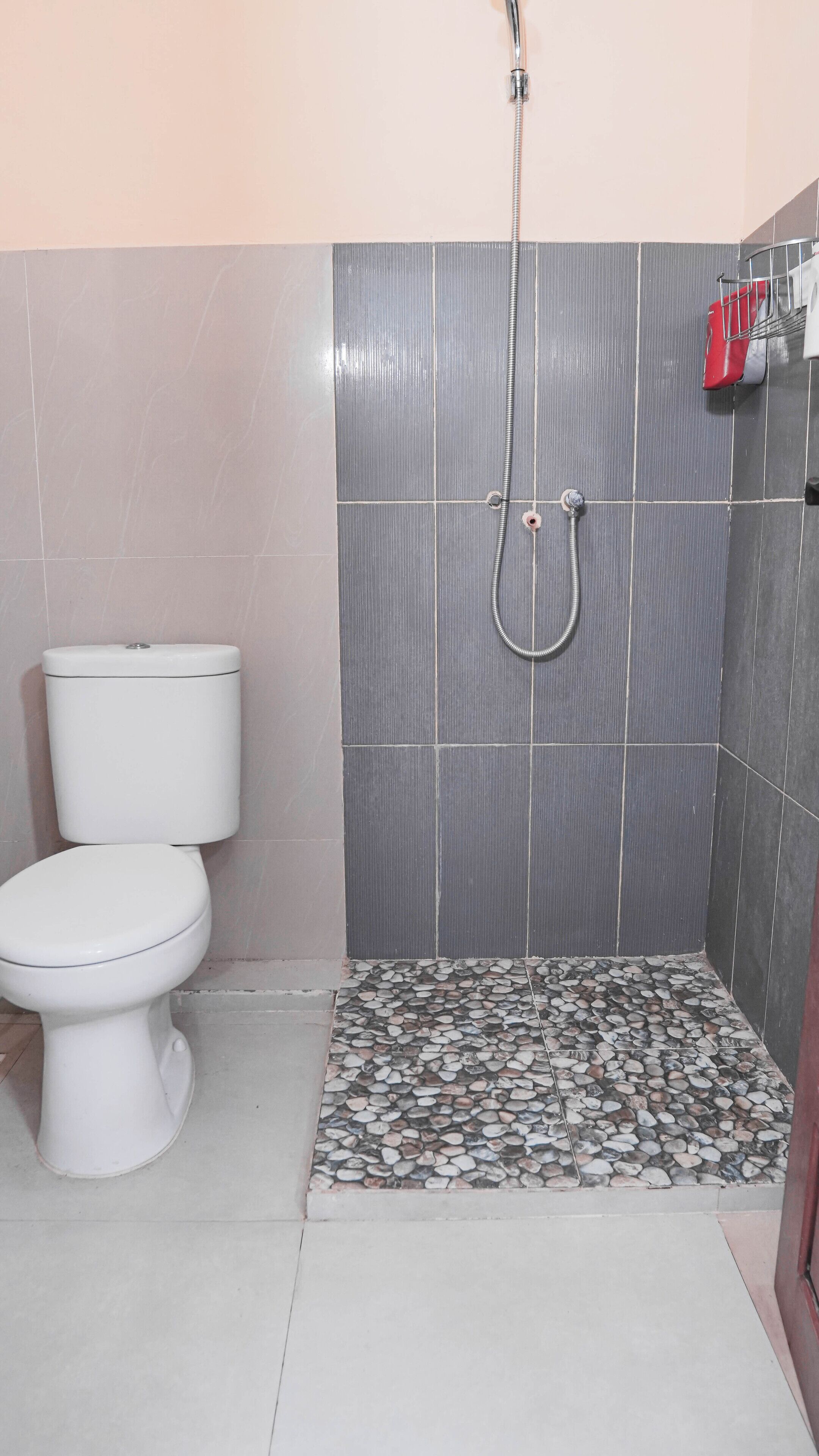 A bathroom with a toilet, a shower with a hose, tiled walls, and a pebble-patterned floor.