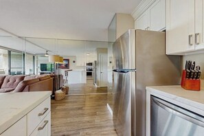 A modern kitchen with a stainless steel refrigerator, wooden flooring, and a dining area with a sofa.