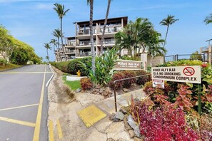 A no-smoking condominium complex with a sign indicating Kihei Alii Kai address, a road with yellow lines, and palm trees.
