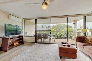 A modern living room with a TV, a sofa, a coffee table, and a balcony with a view of buildings and trees.