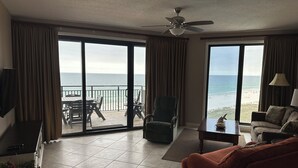 A room with a large sliding glass door to a balcony, a ceiling fan, a sofa, a coffee table, and a TV mounted on the wall.