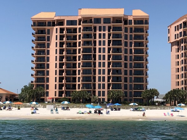 Un hotel de gran altura con varios balcones, una playa en primer plano y sombrillas en la arena.