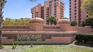 A multi-story hotel with a pink facade, a landscaped area with a wall featuring the name 'SeaChase', and a palm tree.