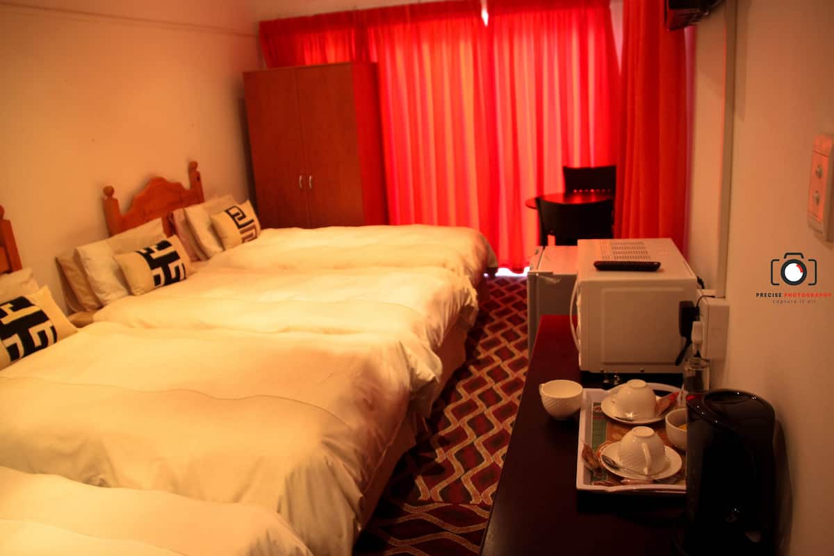 Una habitación de hotel con una cama, un escritorio con cafetera, una silla y un armario.